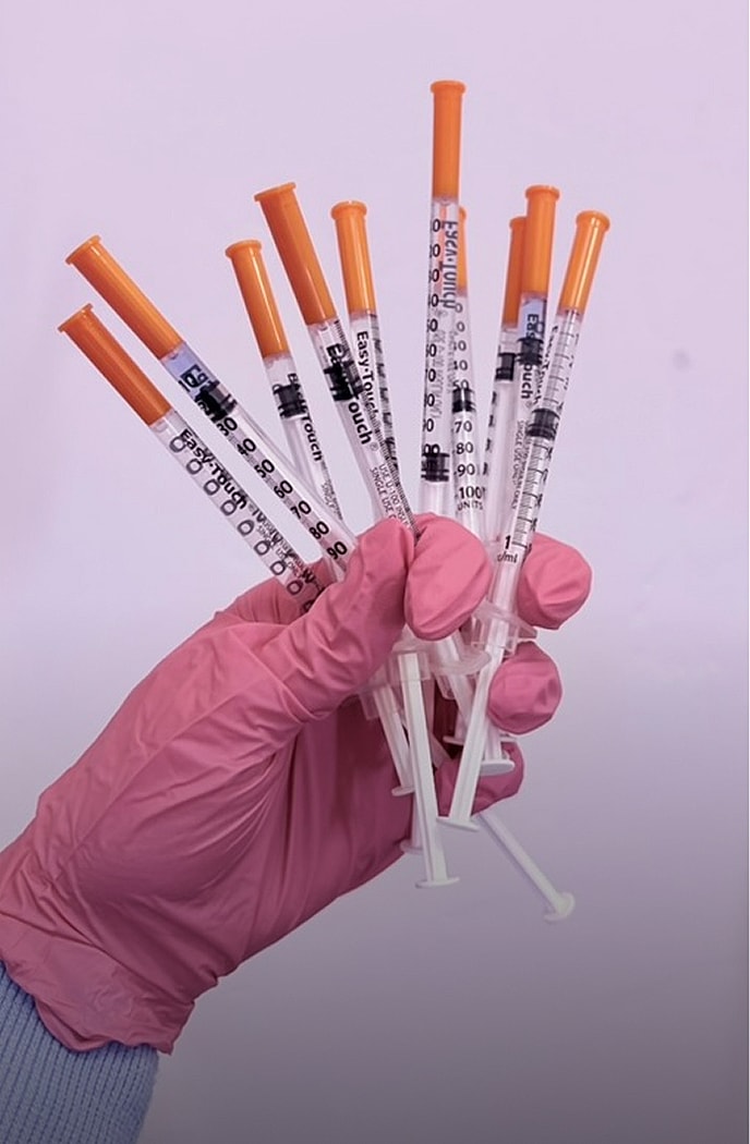 Hand holding multiple syringes with orange caps.