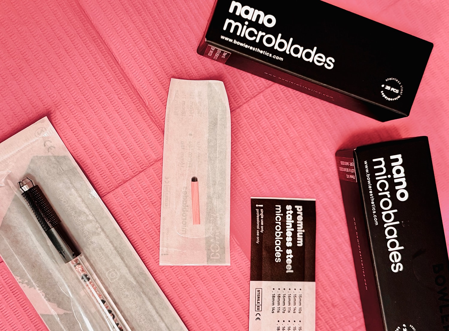Microblading tools arranged on pink background.