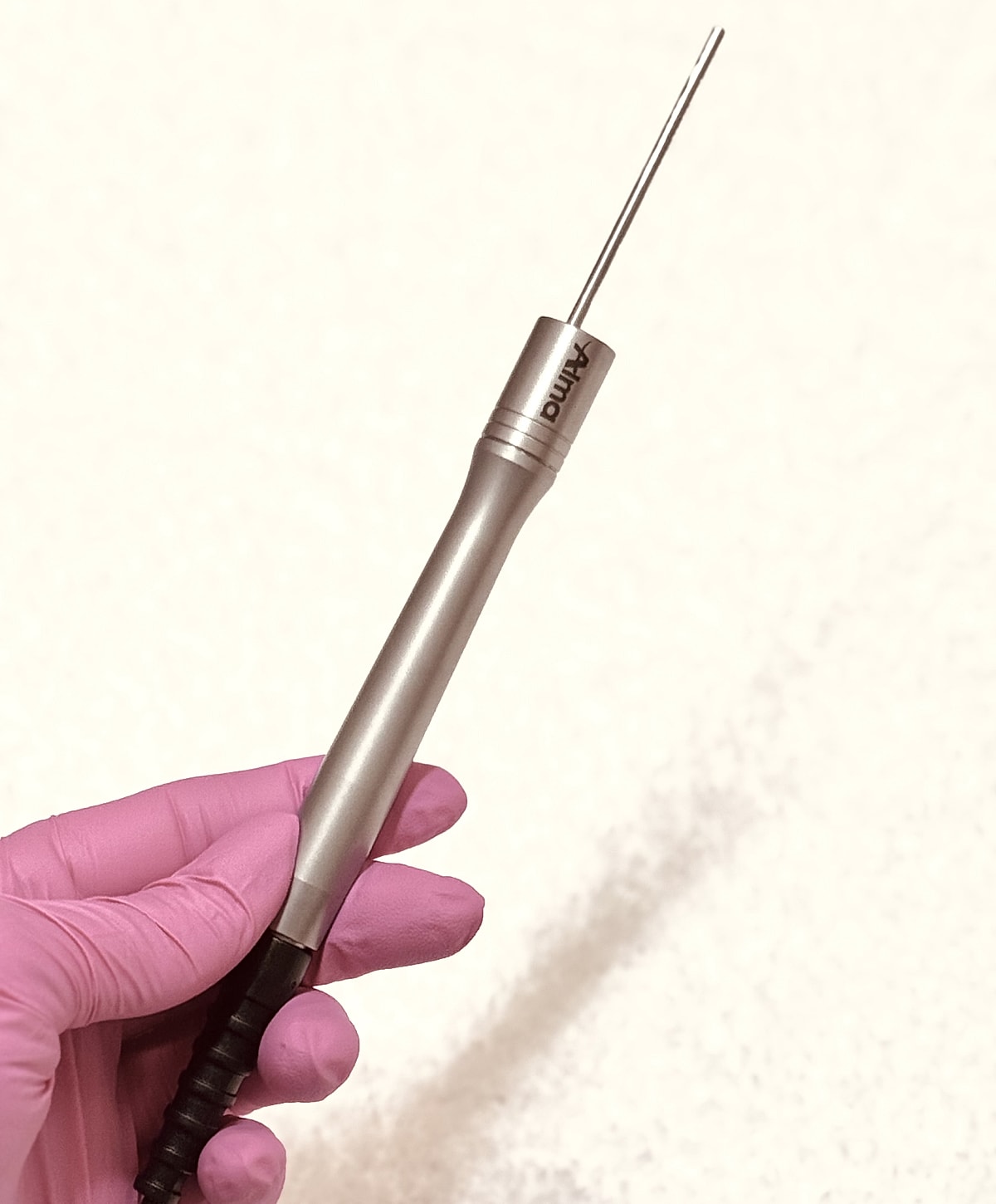 Hand holding a dental tool with pink gloves.