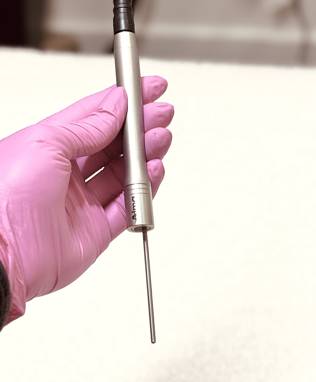 Hand holding a metal probe with pink gloves.